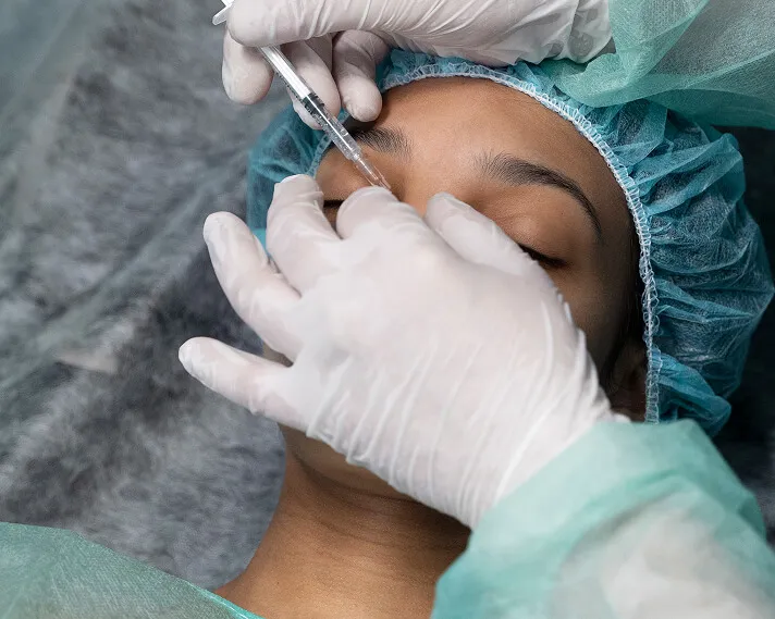 Gloved hands giving a patient a cosmetic injection beside the eye